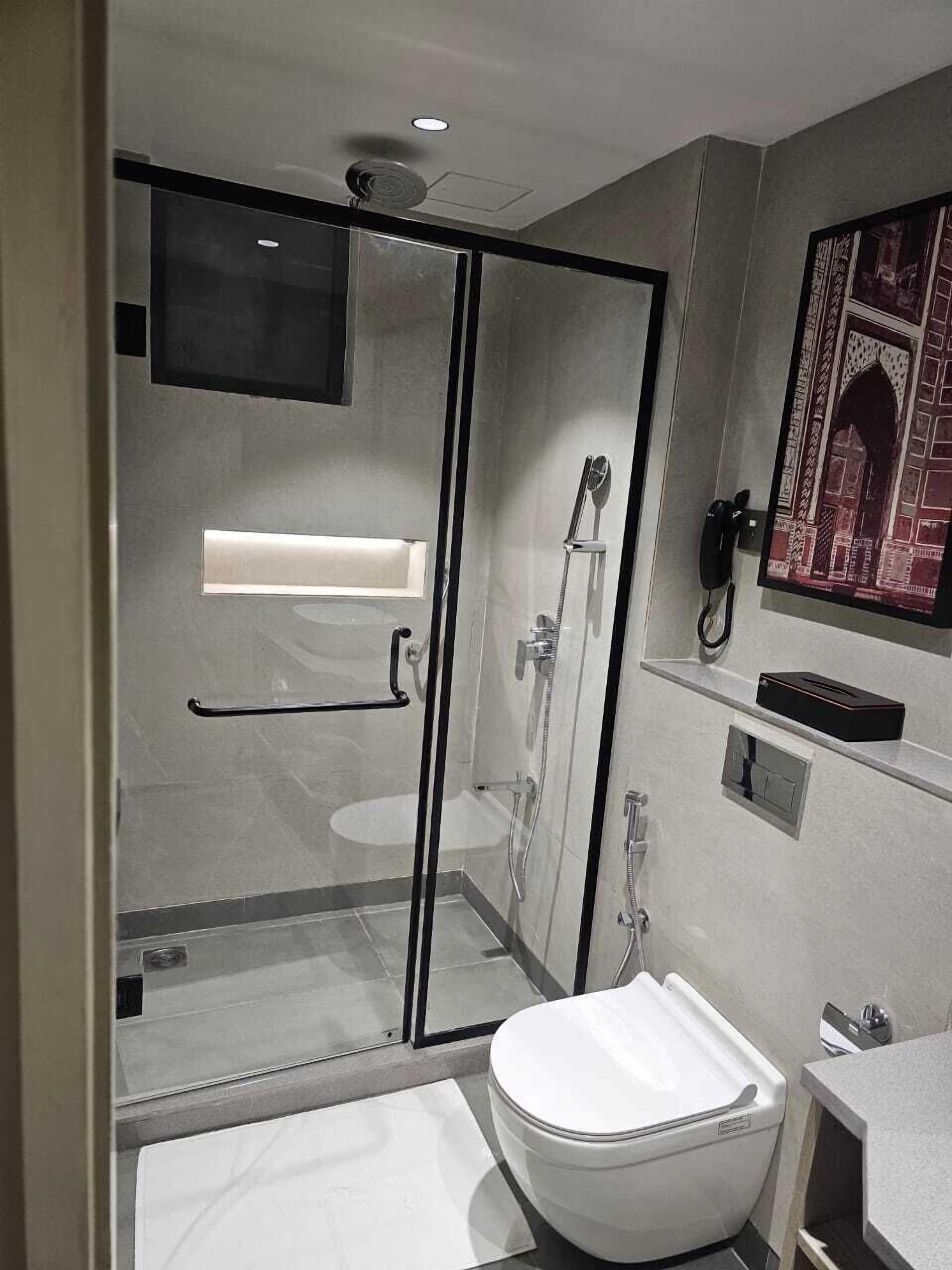 A modern bathroom with a glass shower enclosure, a toilet, a sink, and a mounted phone.