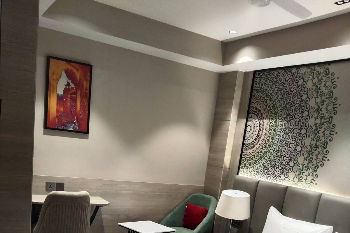 A hotel room with a large bed, a desk, a chair, a lamp, and a tapestry on the wall.