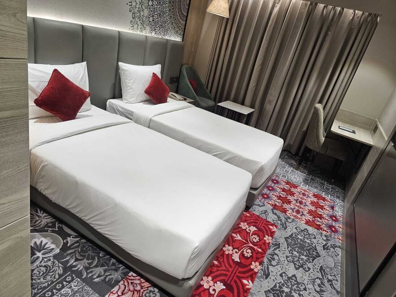 Habitación de hotel con dos camas, un escritorio, una silla y una alfombra estampada.