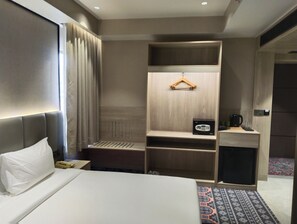 Habitació d'hotel amb un llit, una taula de nit amb un telèfon, un petit armari, una perxa per a abrics i una taula de nit amb una cafetera.