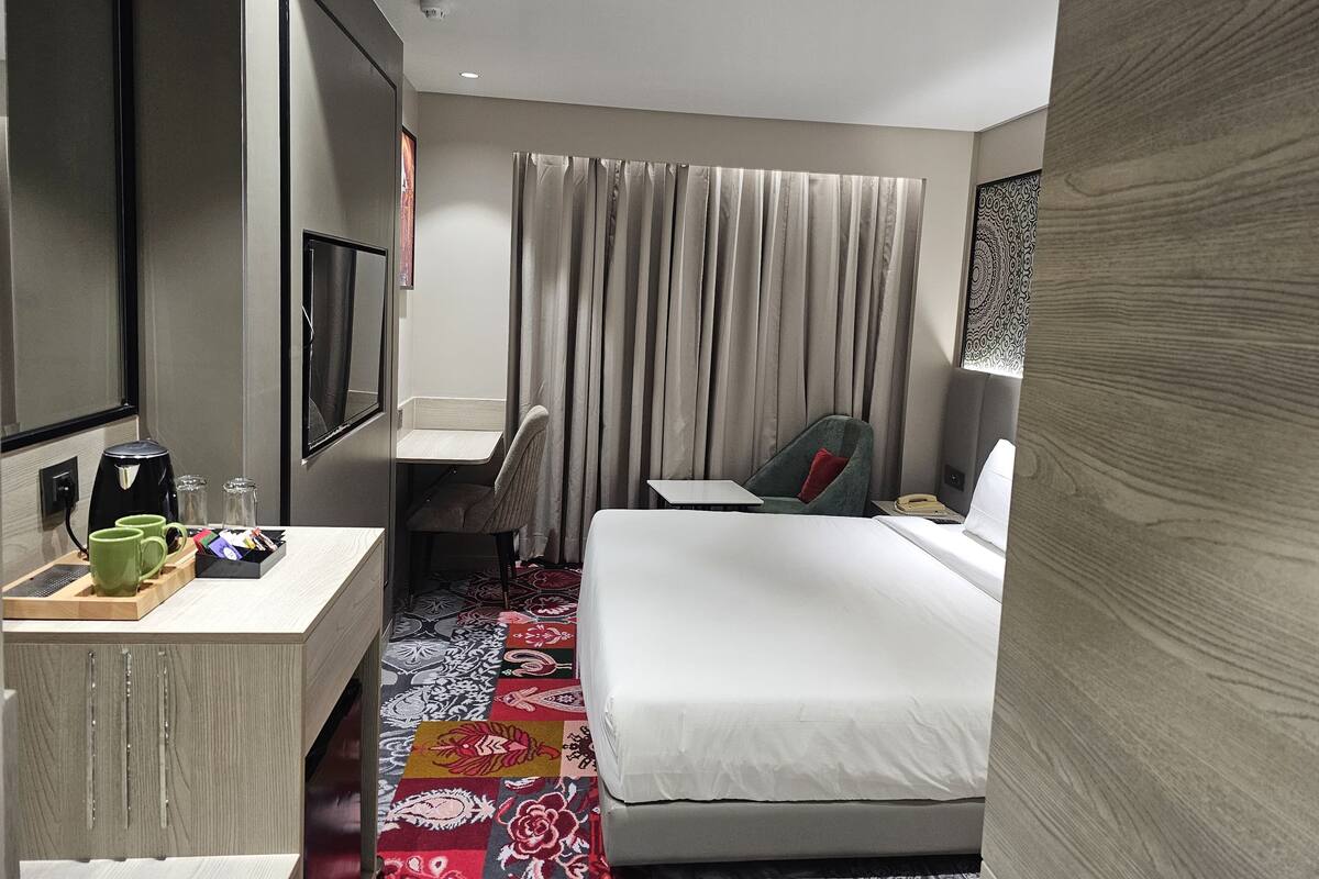 A hotel room with a bed, a desk, a chair, a television, and a coffee maker.