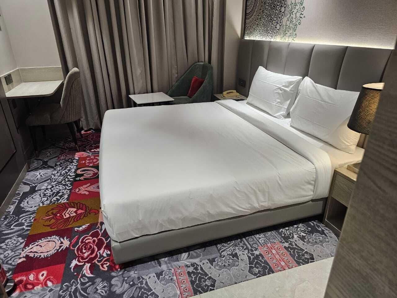 Una habitación de hotel con una cama grande, un escritorio, una silla y una alfombra estampada.