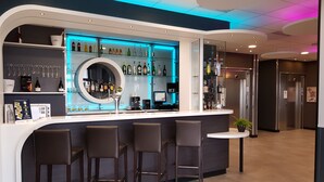 A modern bar area with a curved counter, bar stools, and shelves stocked with bottles and glasses. - B&B HOTEL Béthune Bruay-la-Buissière (Bruay-la-Buissiere)
