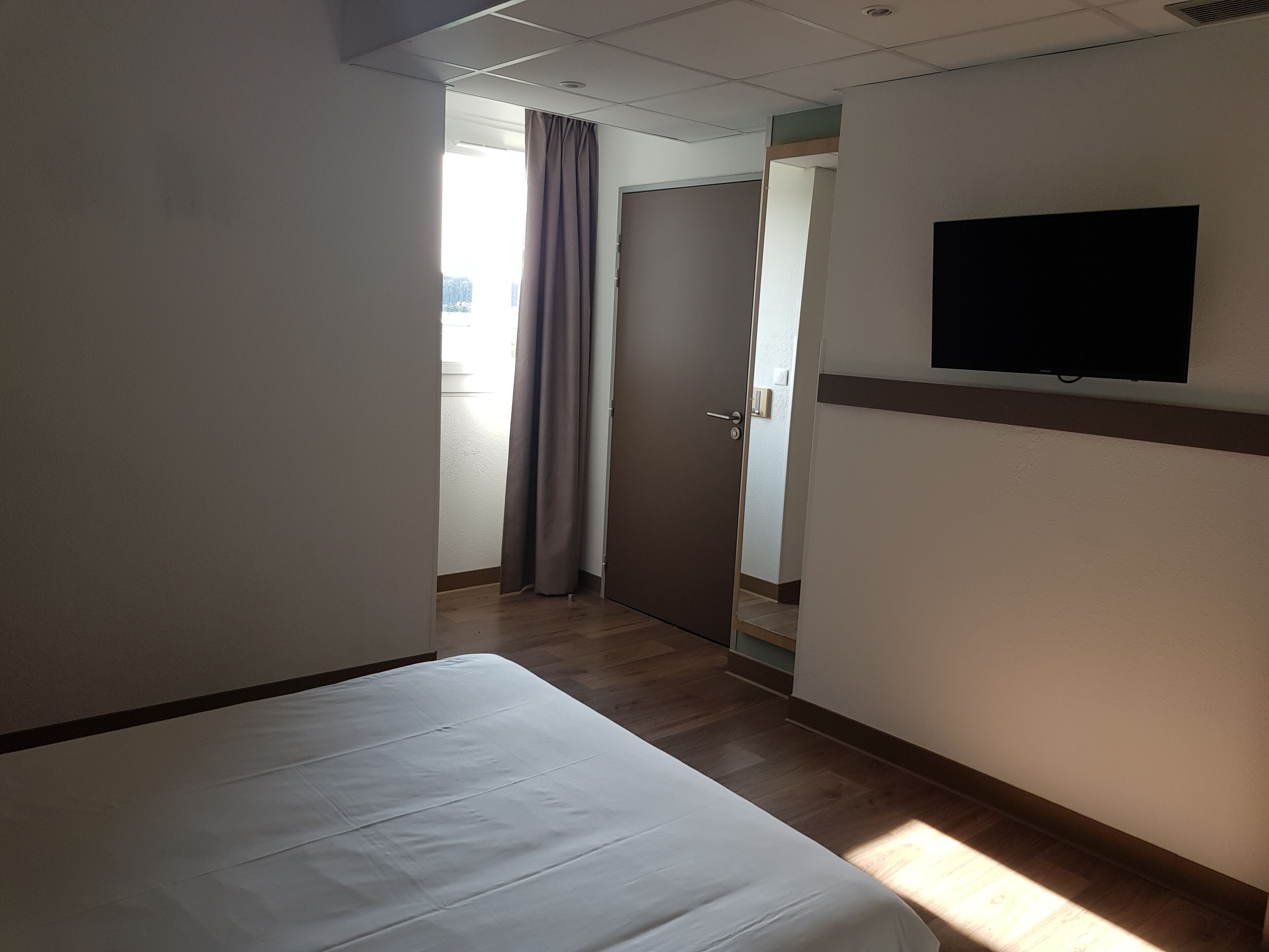 A hotel room with a bed, a television mounted on the wall, and a door leading to another room.