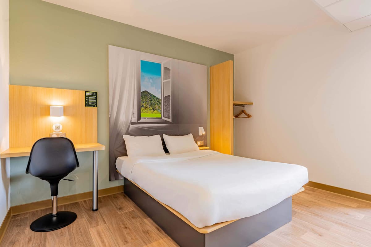Une chambre d’hôtel comprenant un lit, un bureau avec une chaise, une table de chevet et une fenêtre donnant sur une vue sur la montagne.