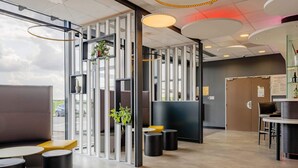 A modern interior with a seating area, a reception desk, and a view of the outdoors. - B&B HOTEL Béthune Bruay-la-Buissière (Bruay-la-Buissiere)