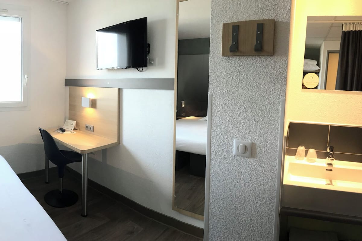Une chambre d’hôtel comprenant un lit, un bureau, une télévision, un miroir et une salle de bain.