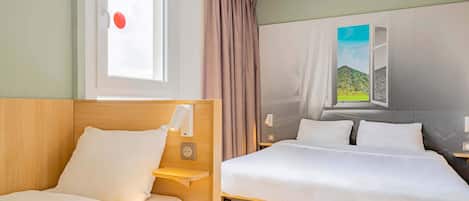 Une chambre d’hôtel avec deux lits, une fenêtre avec des rideaux, une lampe fixée au mur et un tableau représentant un paysage.