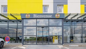 A hotel entrance with a glass facade, a yellow and gray facade, and a sign reading "Bienvenue". - B&B HOTEL Béthune Bruay-la-Buissière (Bruay-la-Buissiere)