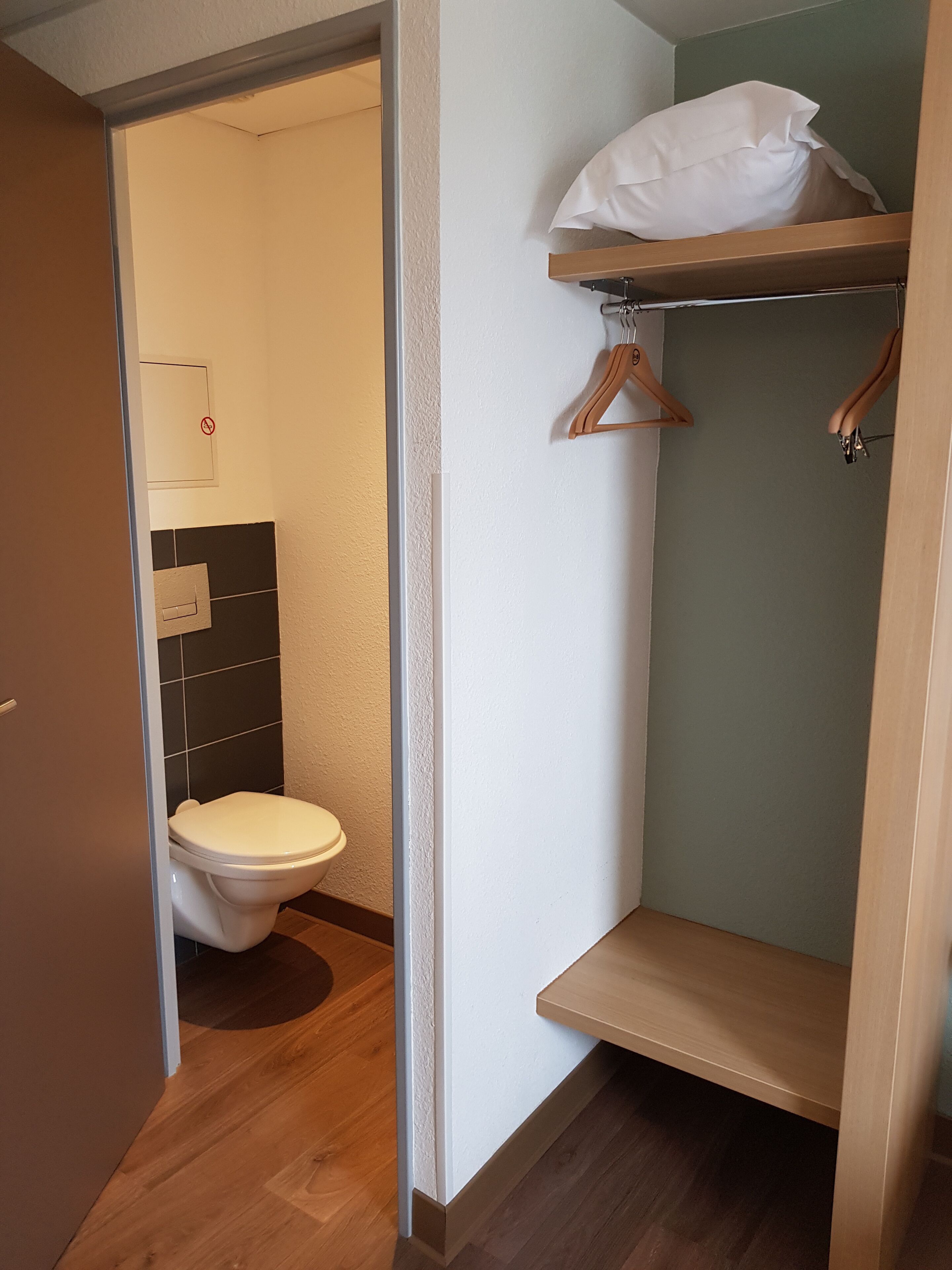 A bathroom with a toilet, a shelf with a white bag, and a wooden hanger.