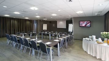 A conference room with a long table, chairs, a whiteboard, a projector screen, and a television.