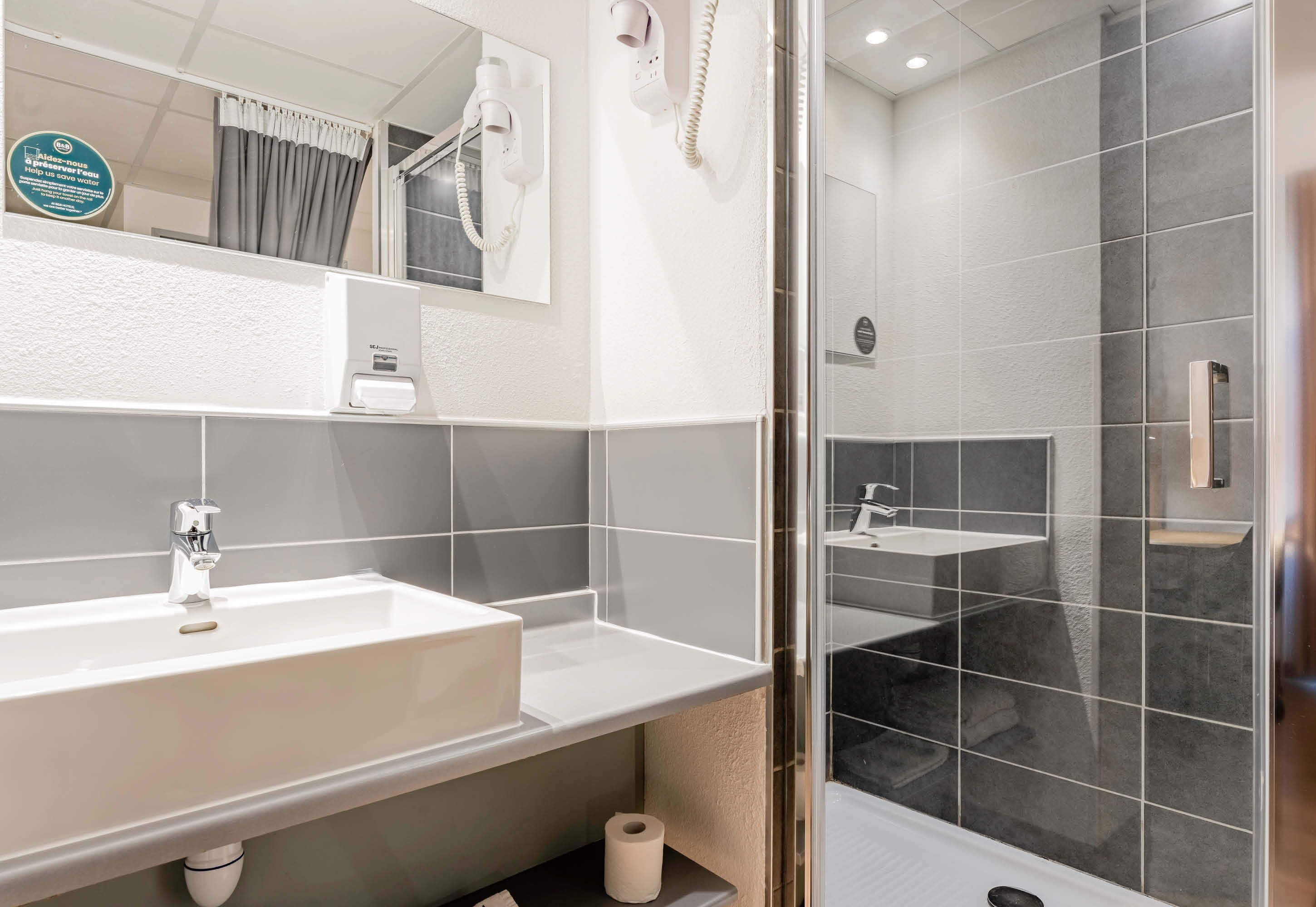A modern bathroom with a white sink, a mirror, a hairdryer, and a shower area.