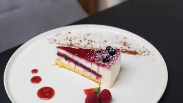Una fetta di dolce stratificato su un piatto bianco, guarnita con frutti di bosco e una spolverata di zucchero, posata su una superficie scura.