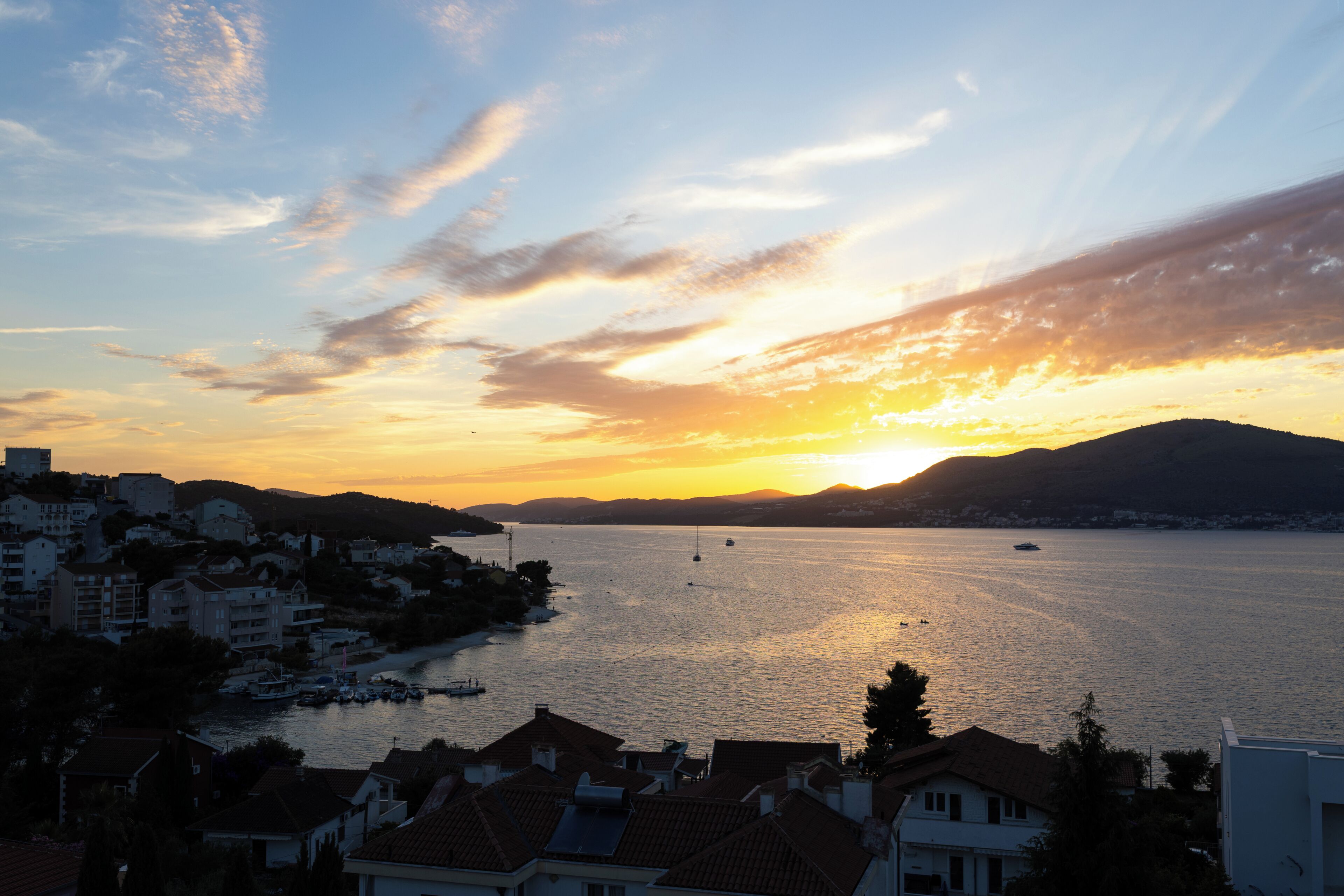 A coastal town at sunset with buildings along the waterfront and boats in the water.