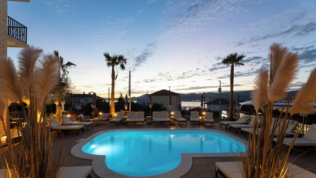Una piscina con sillas de descanso, palmeras y vistas al atardecer.