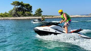 Um jet ski sobre a água, com uma costa rochosa e árvores ao fundo.