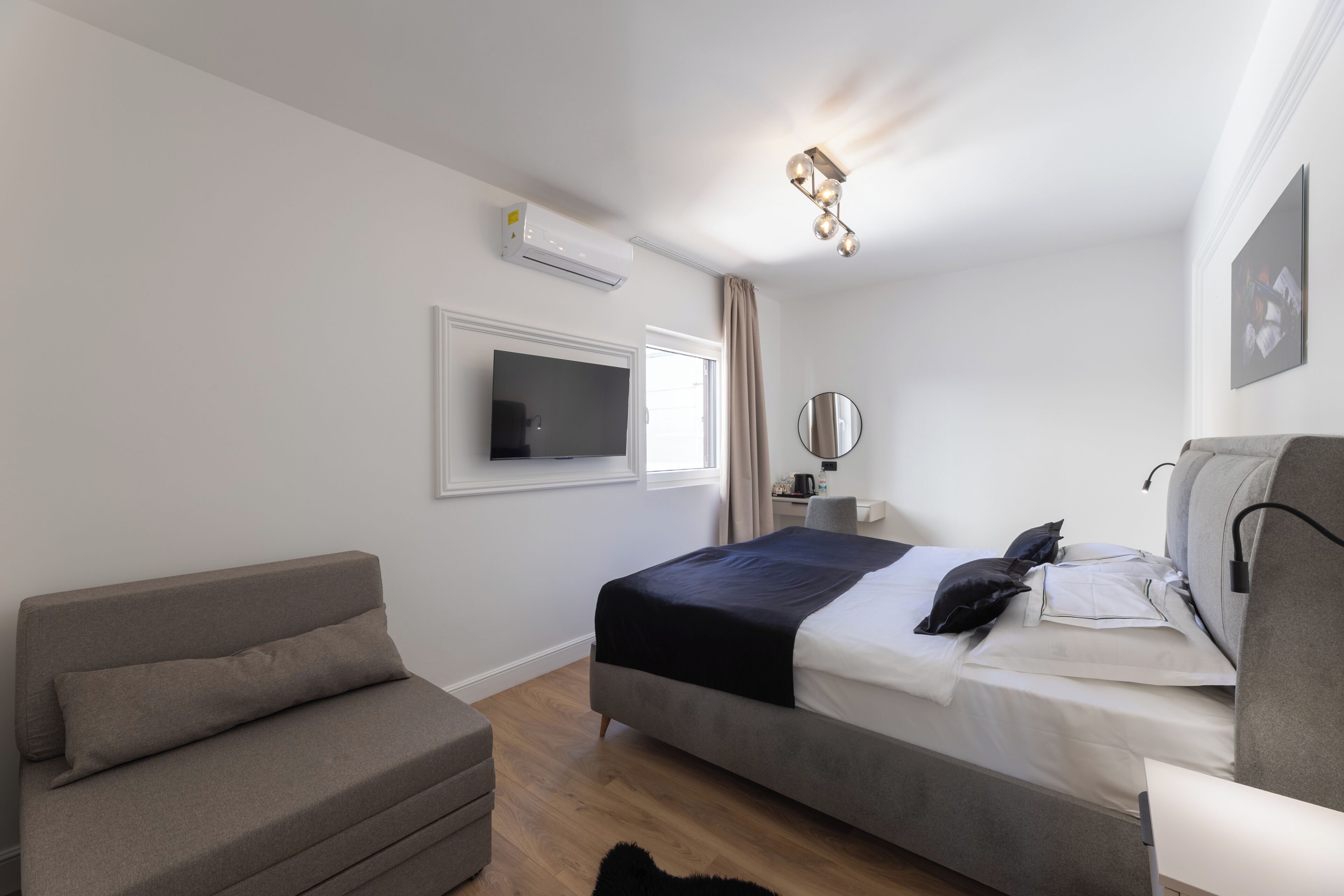 Ein modernes Schlafzimmer mit Bett, Sofa, Fernseher, Klimaanlage, Spiegel und Deckenleuchte.
