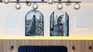 Habitación de hotel con pared de paneles de madera, cabecera tapizada en azul y dos fotografías enmarcadas de paisajes urbanos.