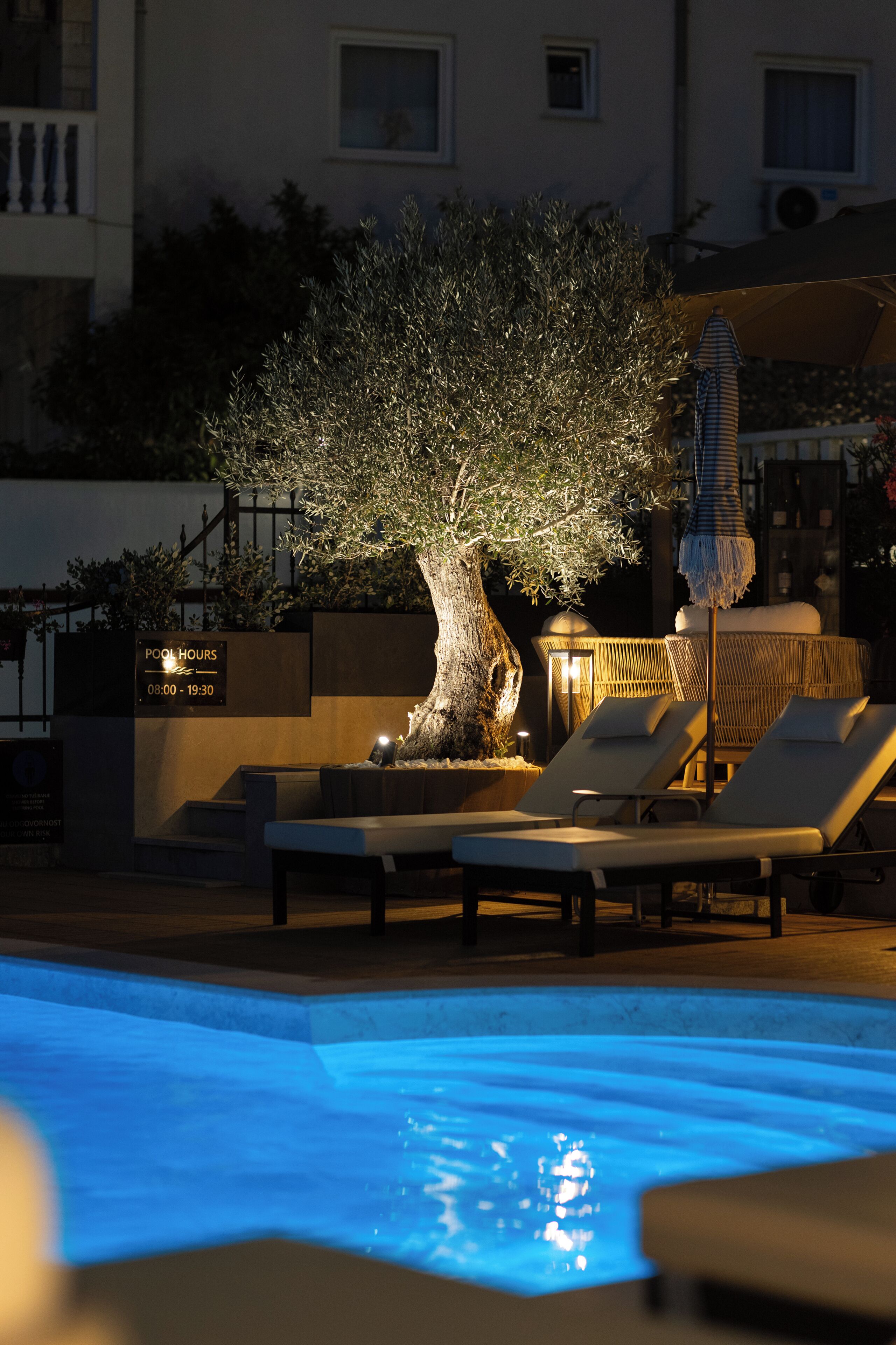 A pool area with lounge chairs, a tree, and a sign indicating pool hours.