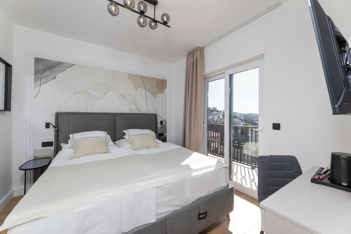 Quarto de hotel moderno com uma cama grande, uma escrivaninha, uma cadeira e uma varanda com vista para a cidade.