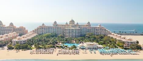 A large resort with multiple buildings, a central pool, and a beach area with umbrellas.