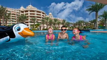 Relax by the pool with a fun float, surrounded by lush palm trees and the hotel's grand facade.