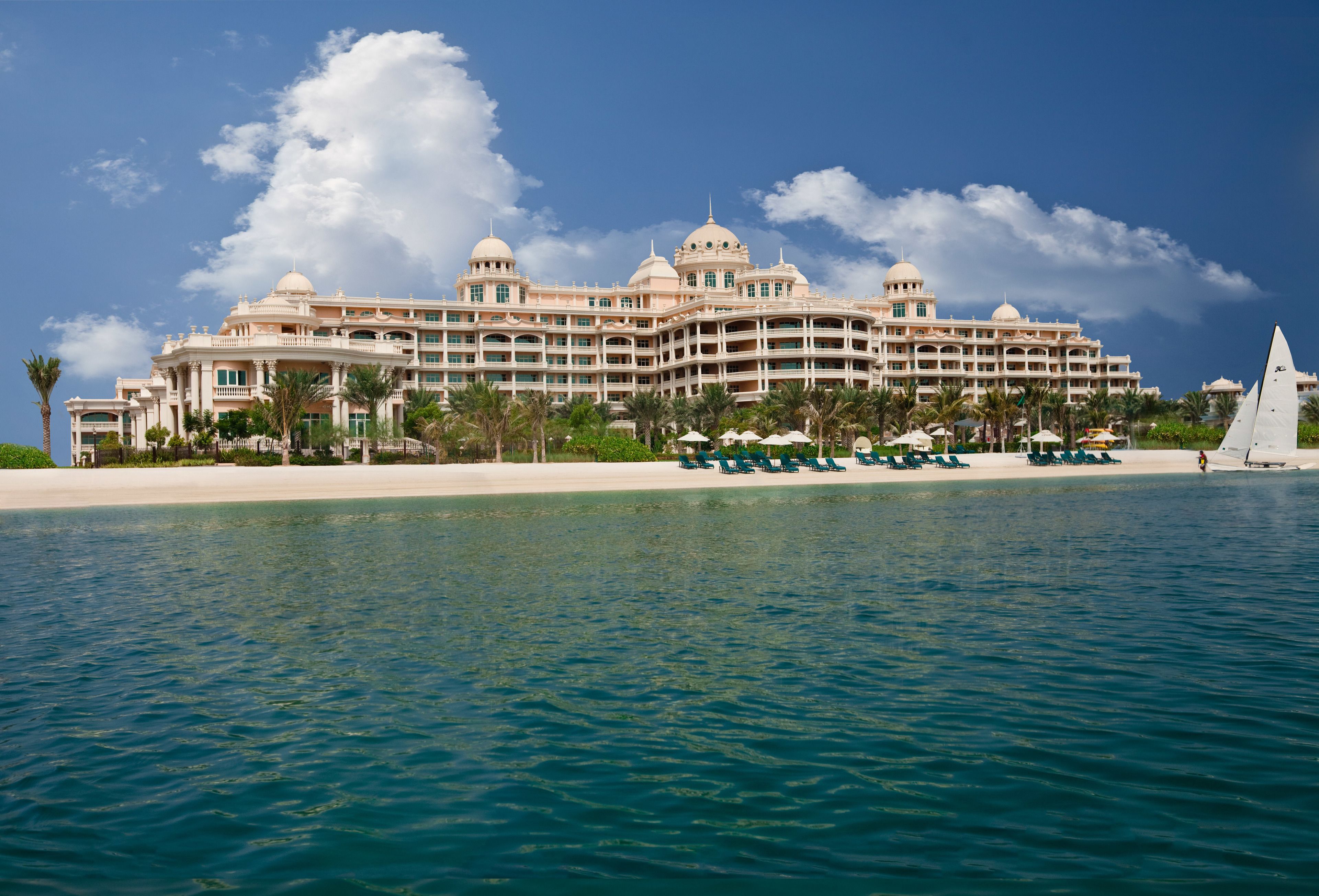 A large, multi-story hotel with a beachfront location, featuring a pool area and several lounge chairs.