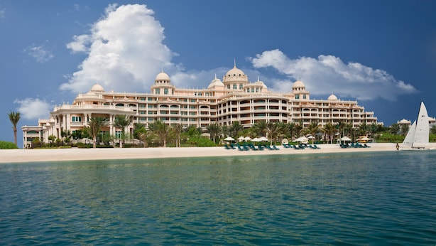 A large, multi-story hotel with a beachfront location, featuring a pool area and several lounge chairs.