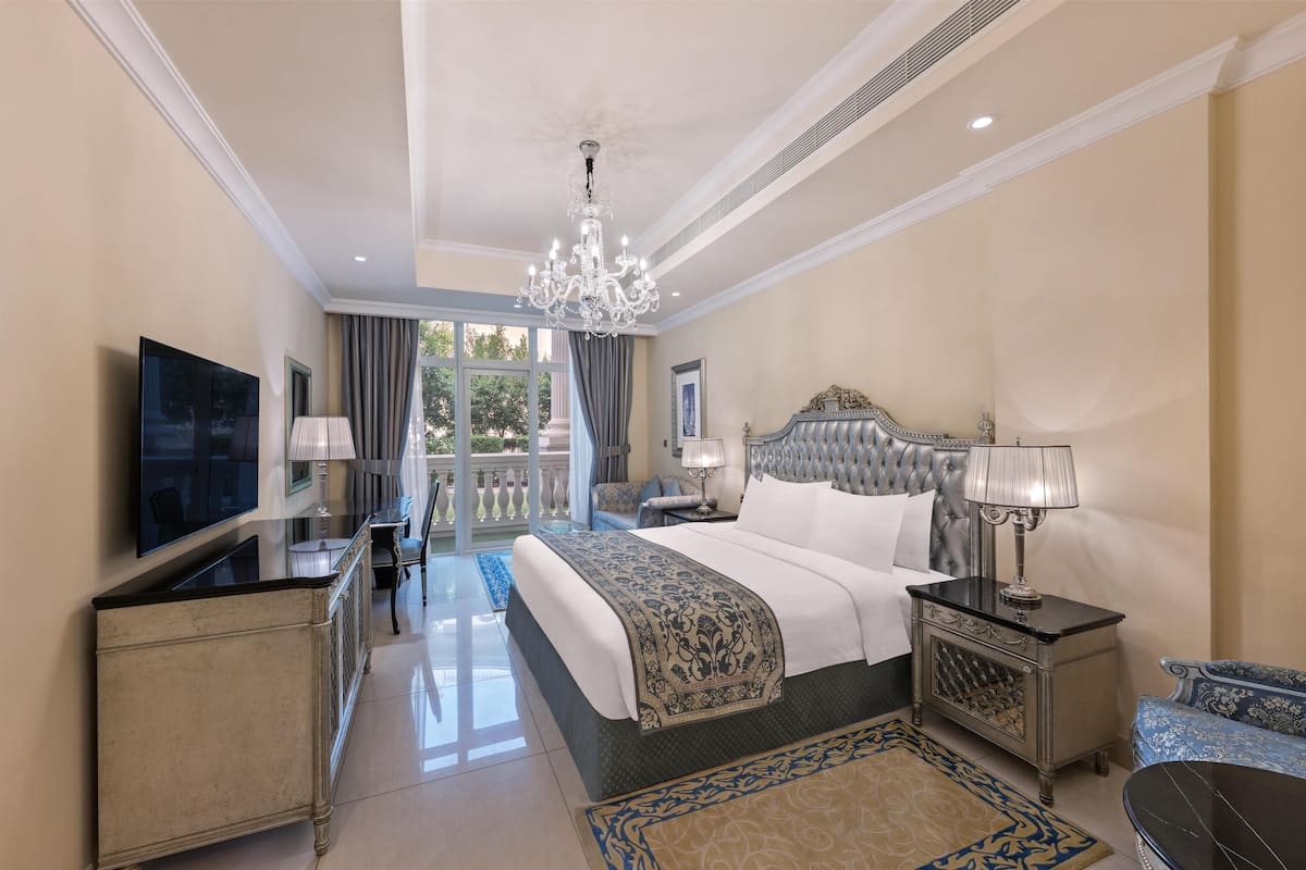 A spacious bedroom with a large bed, a television, a chandelier, and a balcony view.