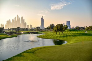 A golf course with a water feature and a city skyline in the background.