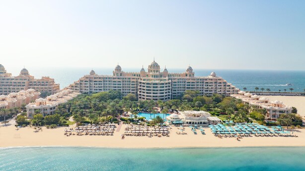 Un gran resort con varias edificaciones, una piscina central y una zona de playa con sombrillas.
