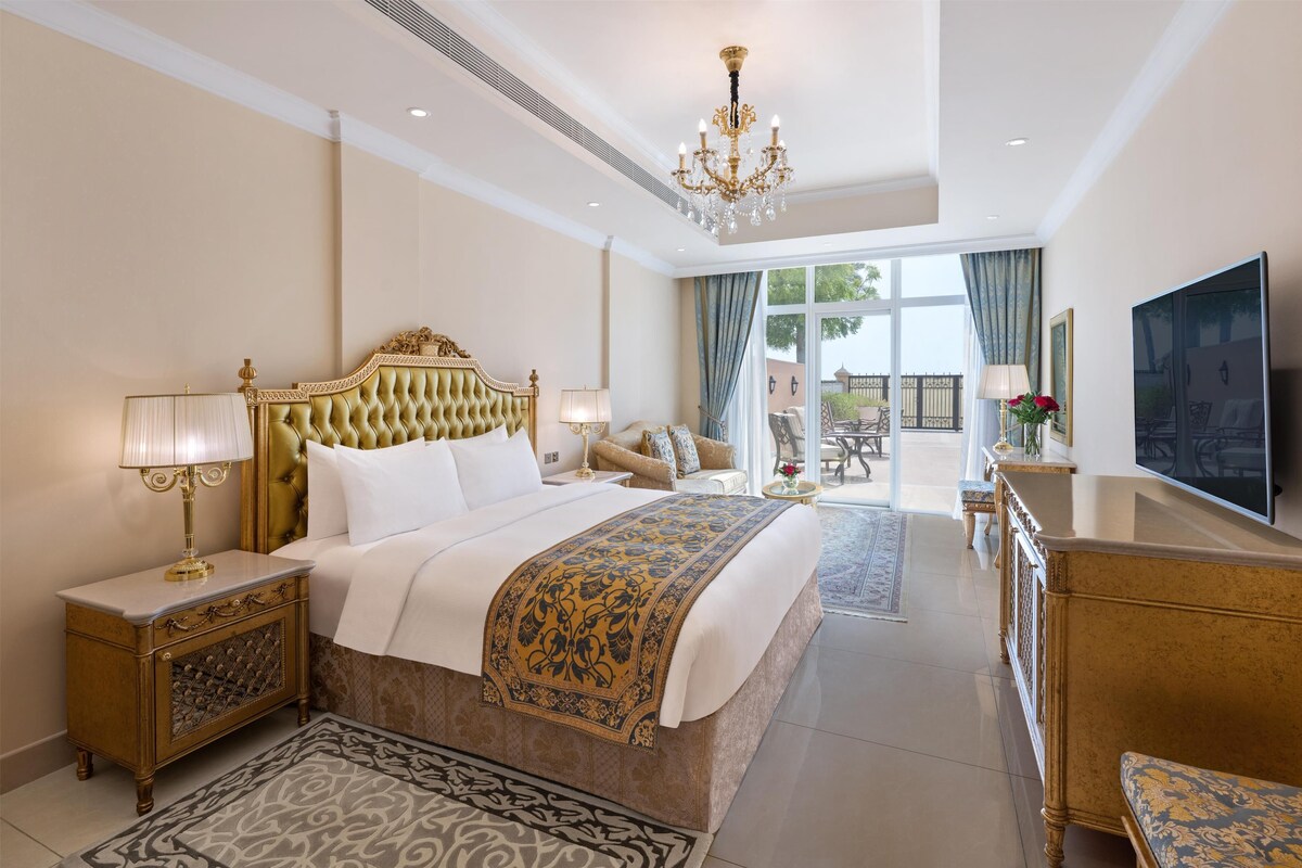 A spacious bedroom with a large bed, a chandelier, a television, and a view of the outdoors.
