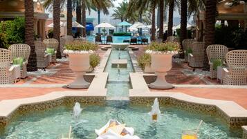 A poolside dining area with a table set for breakfast, surrounded by palm trees and a view of a swimming pool.