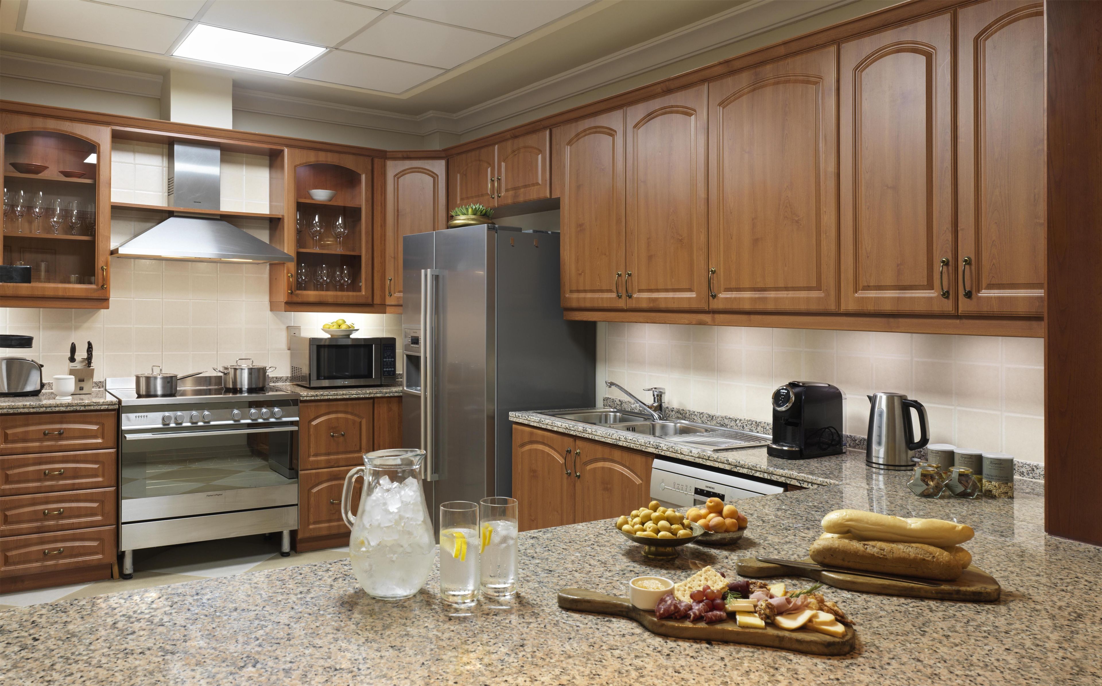 A kitchen with wooden cabinets, stainless steel appliances, granite countertops, and a variety of food items.
