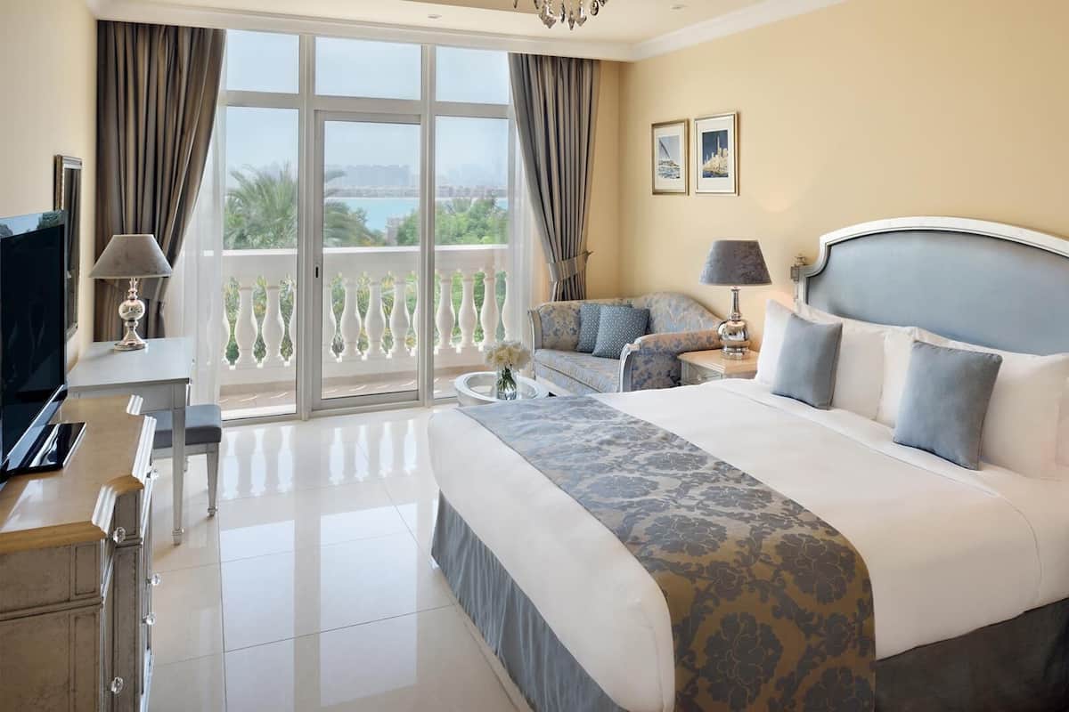 A hotel room with a large bed, a TV, a desk, and a balcony with a view of the city.
