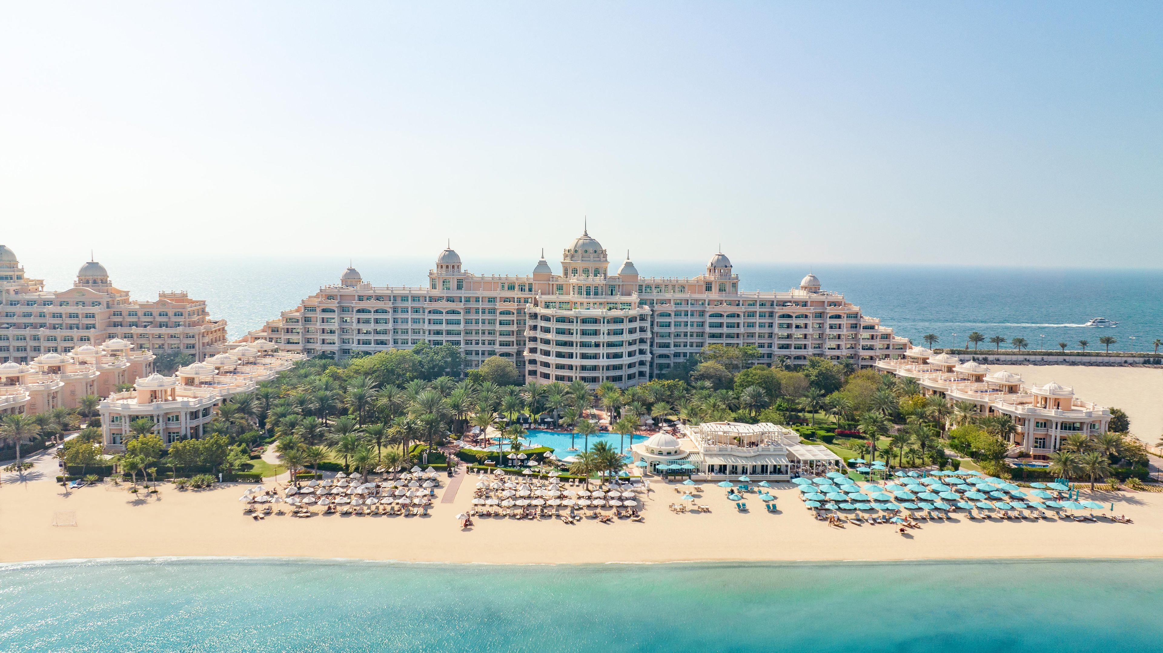 A large resort with multiple buildings, a central pool, and a beach area with umbrellas.