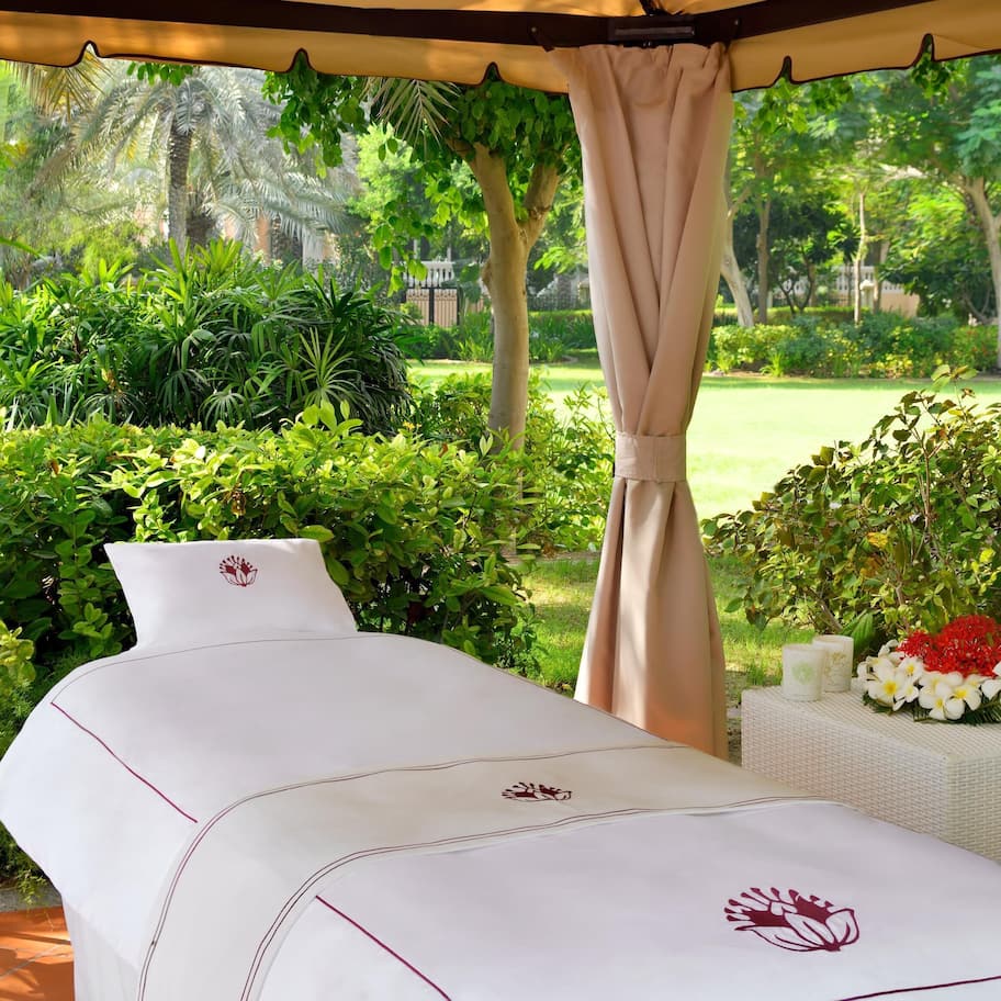 A spa bed with a canopy, surrounded by lush greenery and a garden view.
