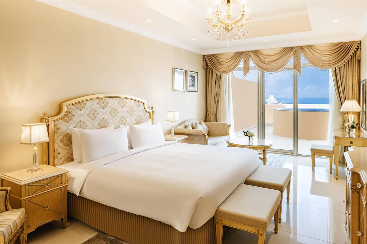 A luxurious bedroom with a large bed, a chaise lounge, a desk, and a view of the ocean.