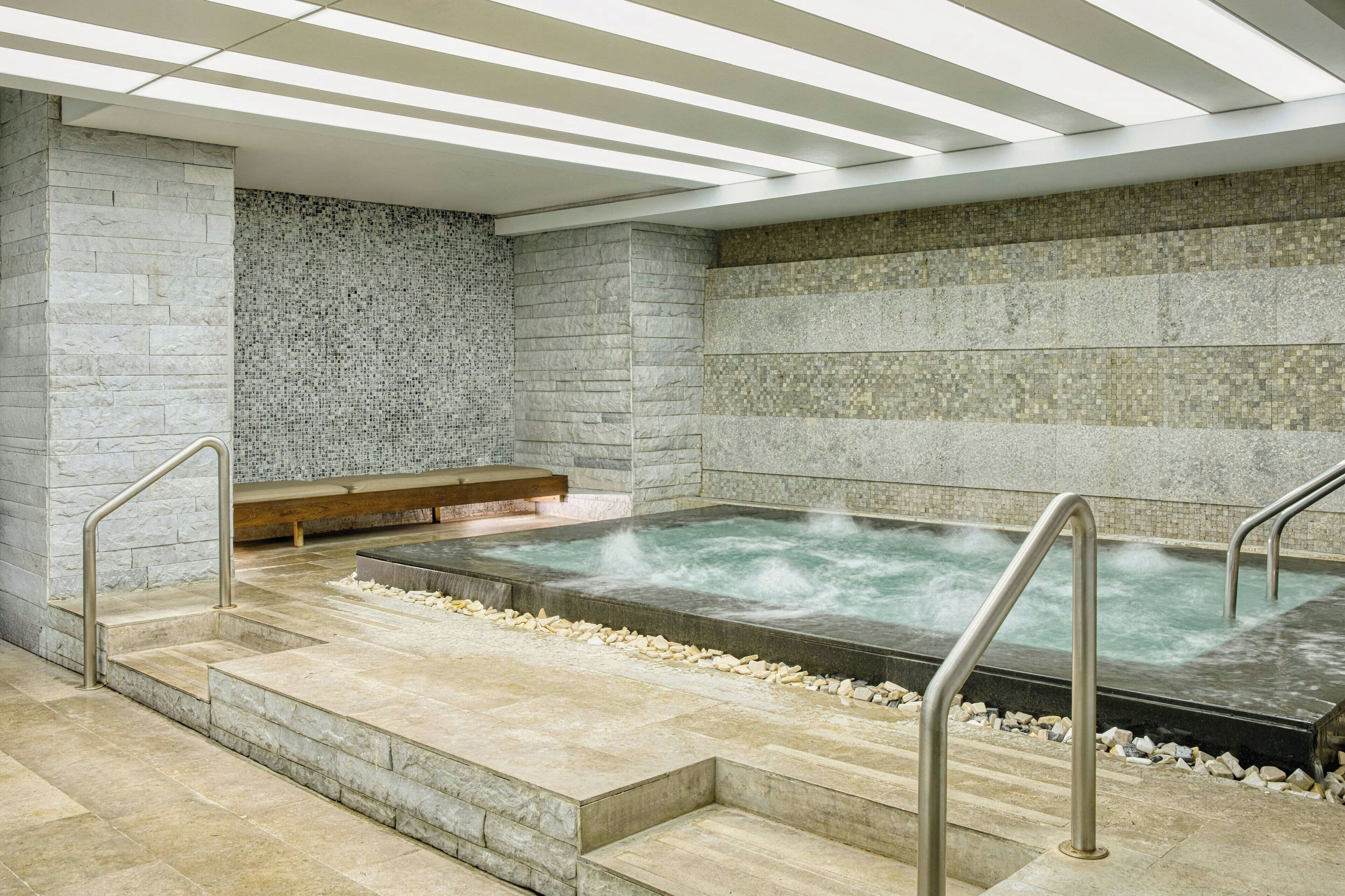A spa area with a hot tub, stone walls, and a wooden bench.