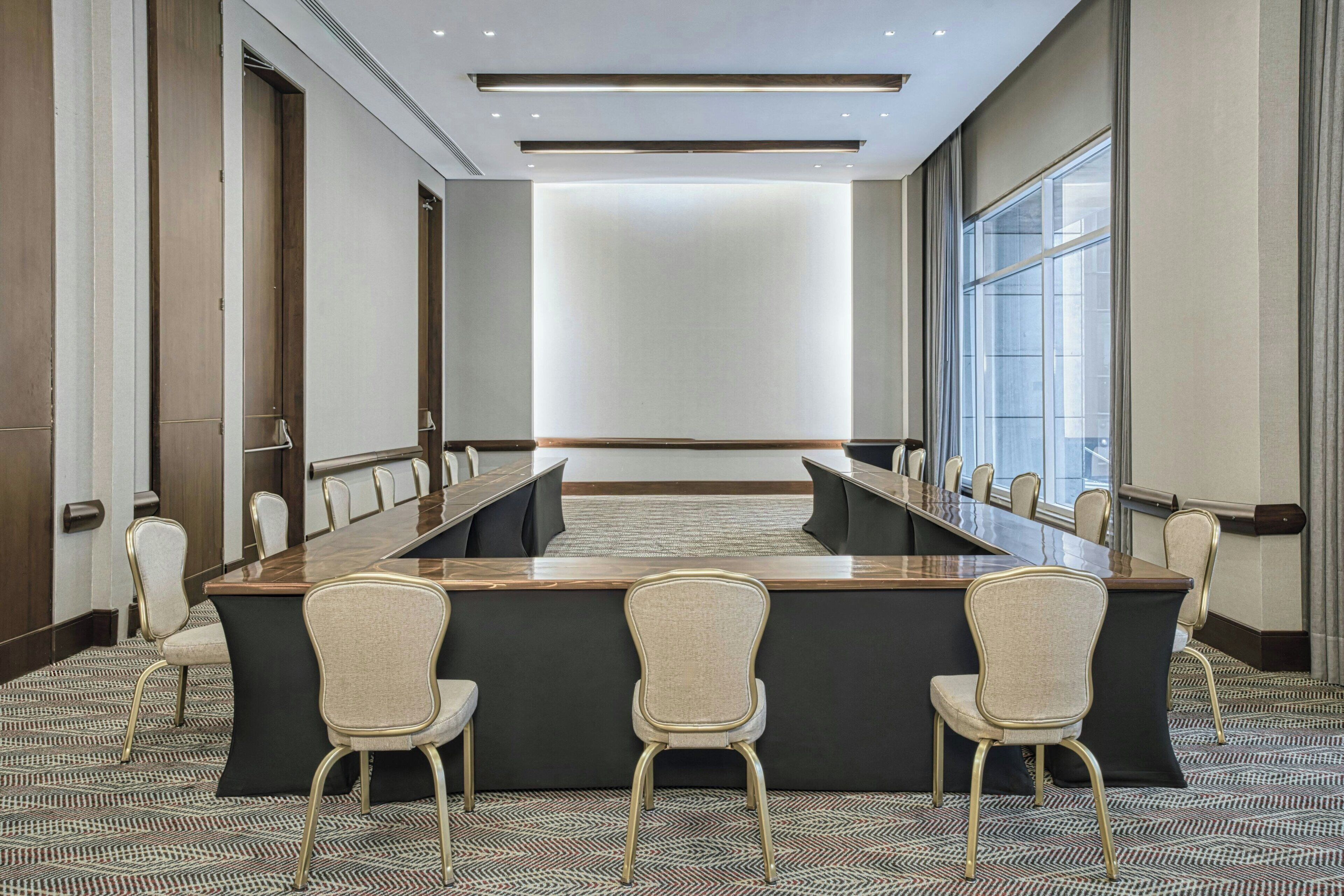 A conference room with a long table and chairs, large windows, and a patterned carpet.
