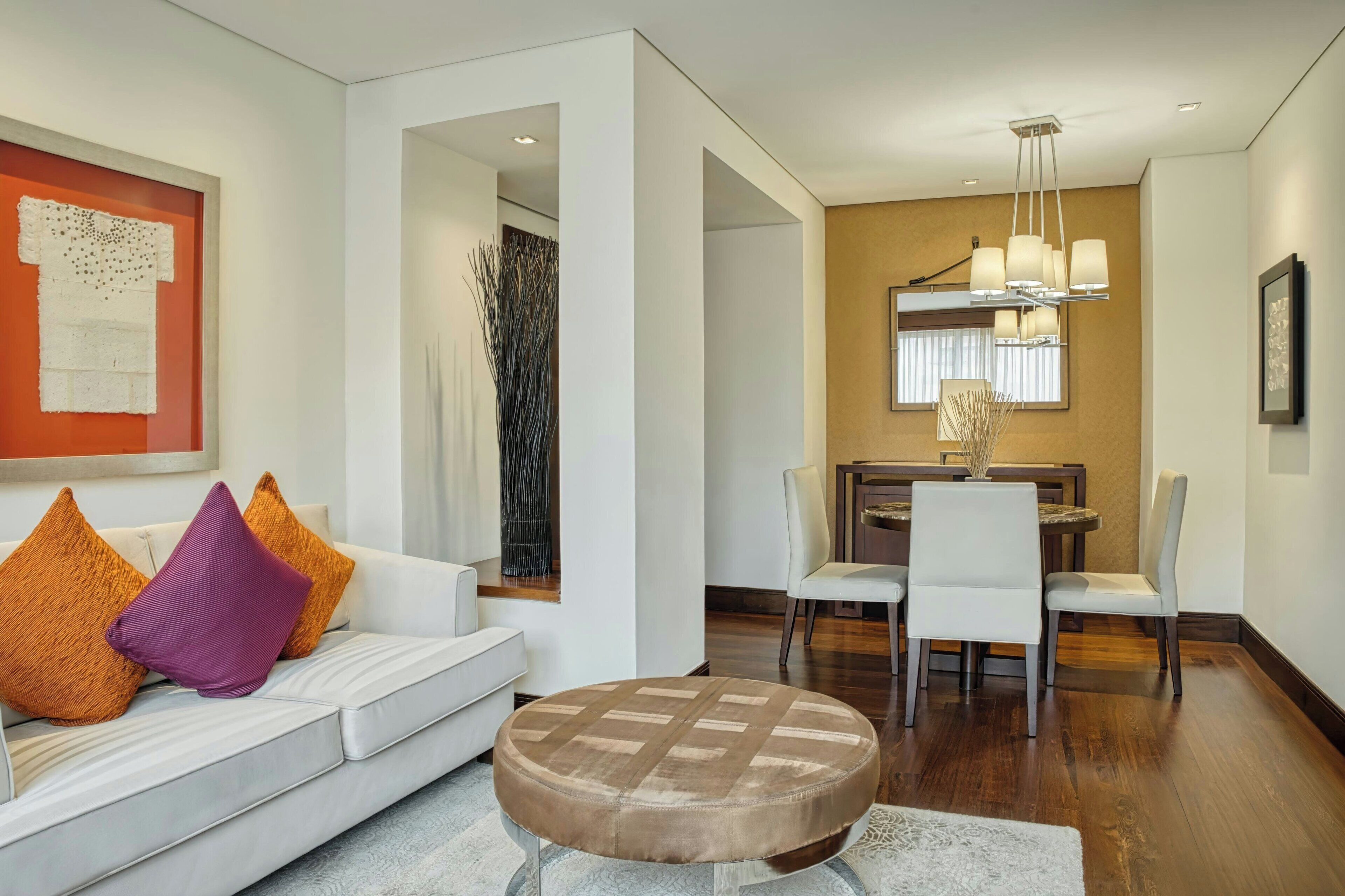 Un salon moderne avec un canapé blanc, un pouf rond et un coin repas comprenant une table et des chaises.