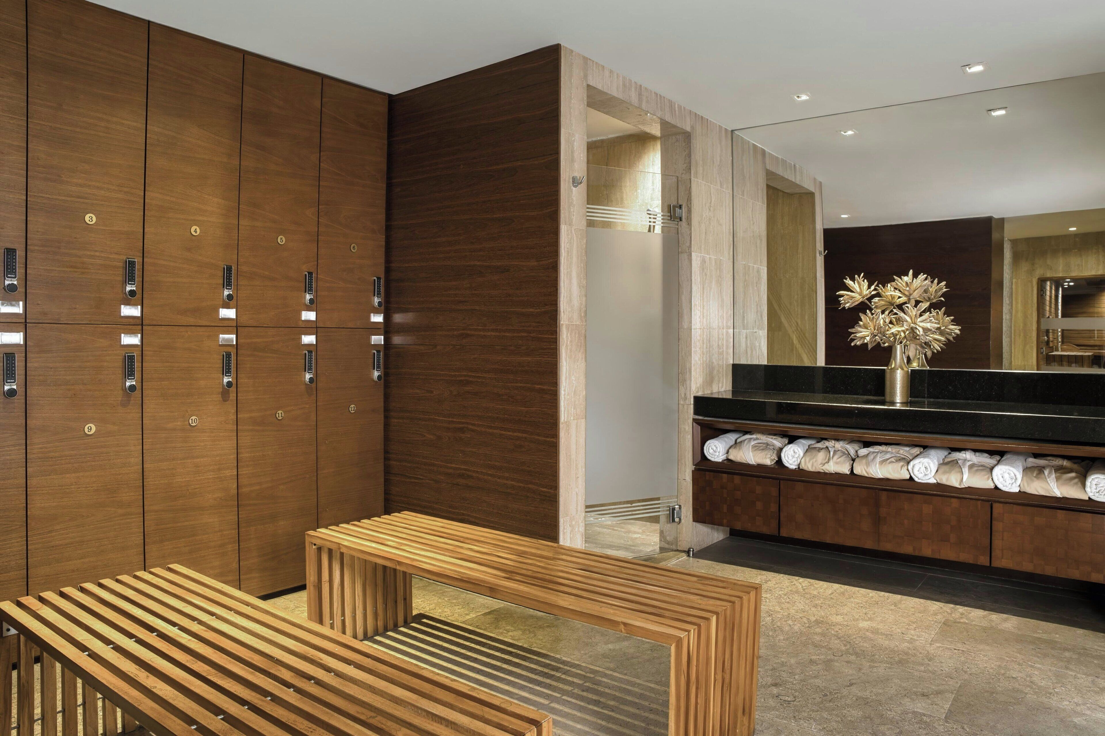 A modern bathroom with wooden lockers, a bench, and a vanity with towels.