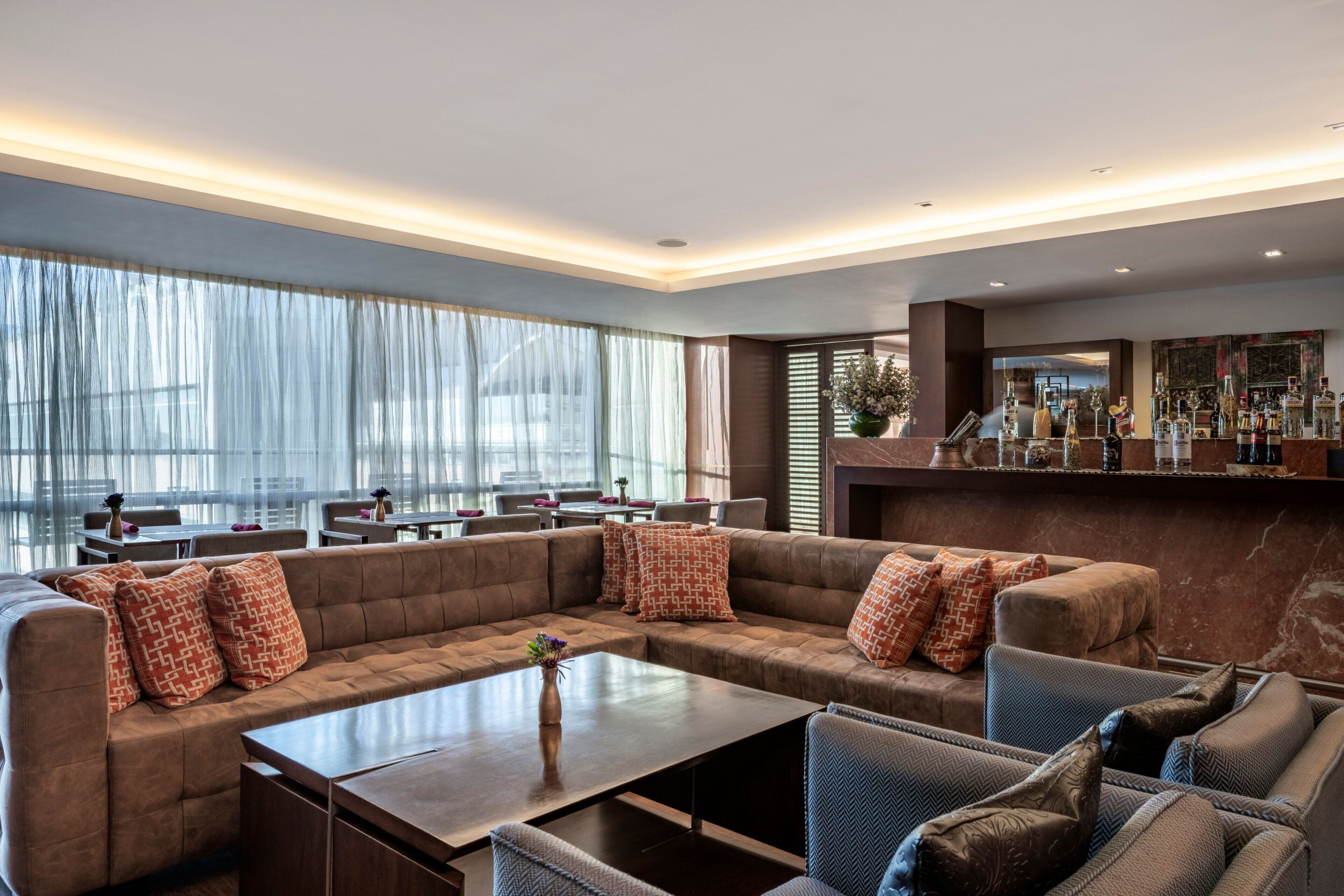 Ein stilvoller Lounge-Bereich mit einer großzügigen Eckcouch, einem Couchtisch und einer Bar mit verschiedenen Flaschen.