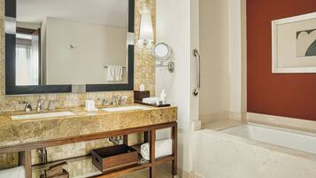 A bathroom with a double sink, a large mirror, a vanity with a wooden base, a towel rack, and a bathtub.