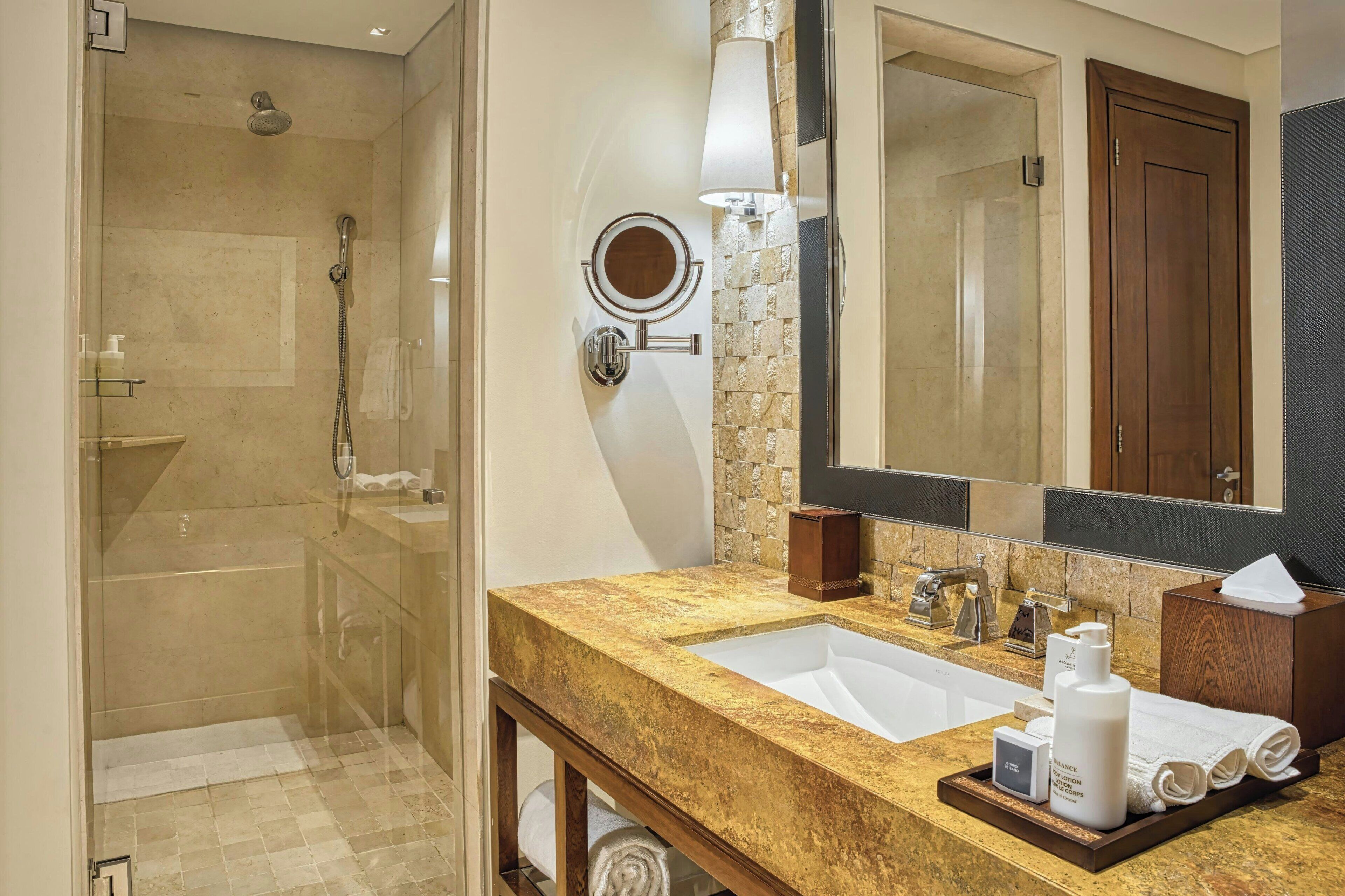 Une salle de bain dotée d’une douche à parois de verre, d’un lavabo avec un plan de toilette en marbre, d’un miroir et d’un meuble-lavabo en bois.