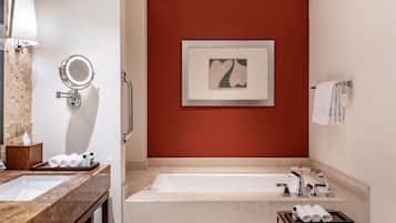 A modern bathroom with a large mirror, a framed artwork on the wall, a bathtub, and a vanity with a tray of towels.