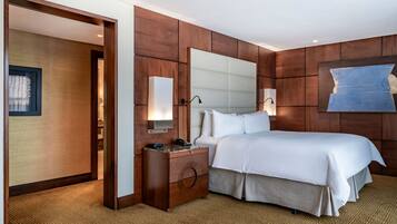 A hotel room with a large bed, a nightstand, a mirror, and a wall-mounted light fixture.