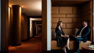 Un vestíbulo de hotel con un largo pasillo, una zona de estar con un sofá y una mesa redonda, y un pilar decorativo.