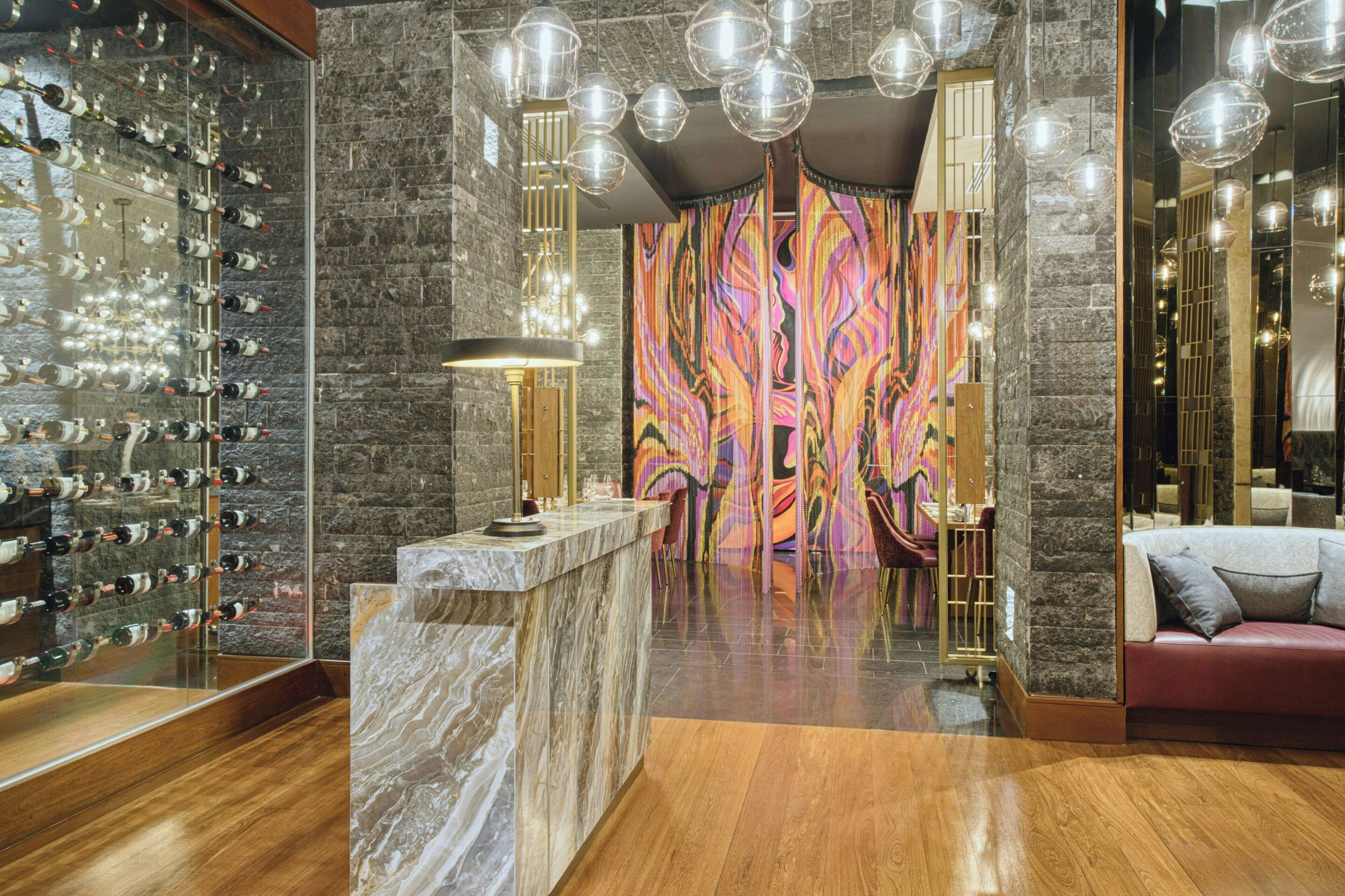 Un vestíbulo con una cava de vinos, mostrador de mármol, un mural de colores y un sofá rojo.