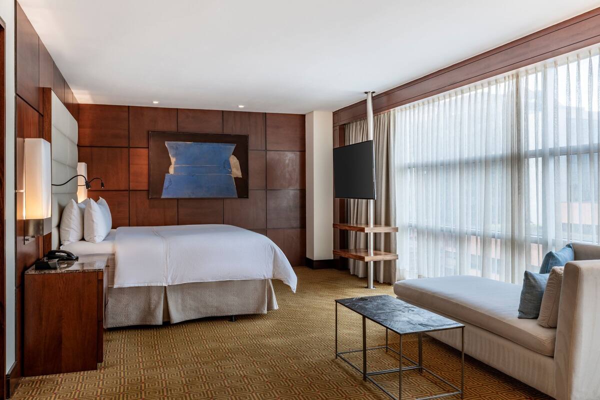 A hotel room with a large bed, a sofa, a TV, and a window with curtains.